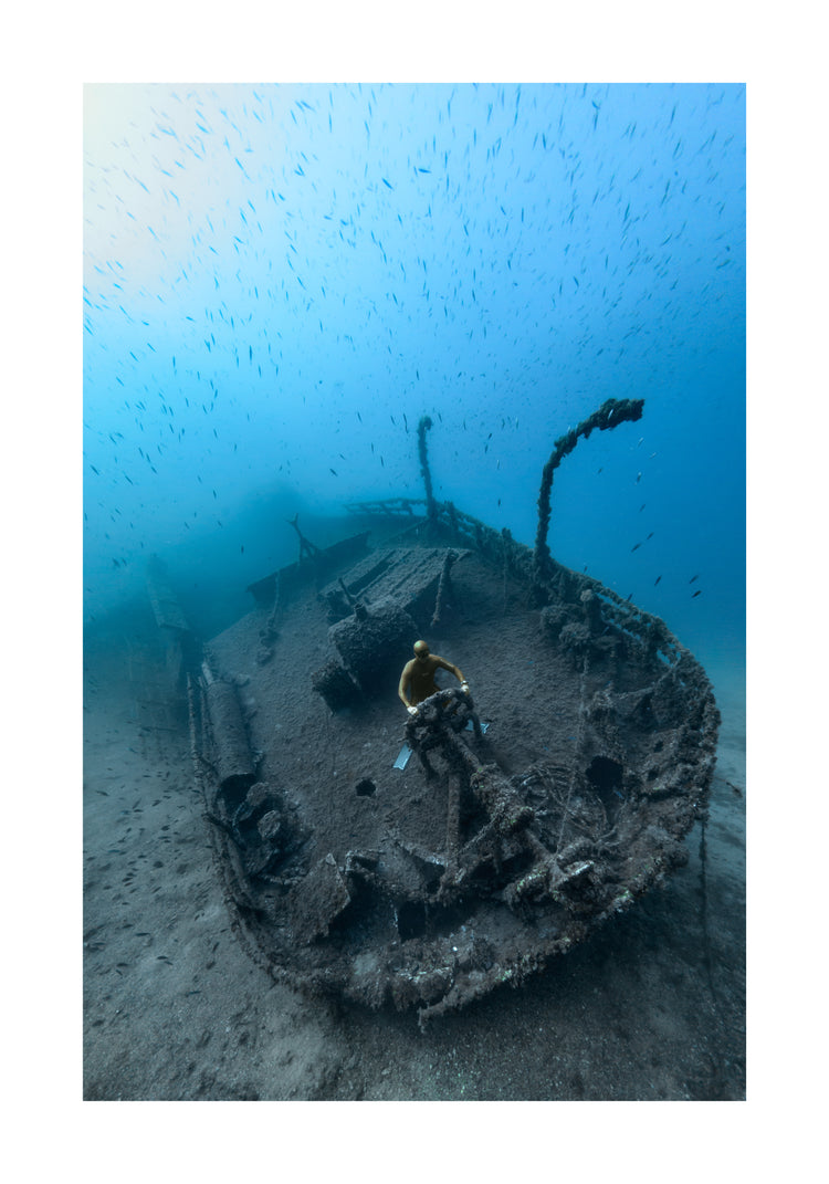 Shipwreck on the bottom of a deep blue ocean with a diver behind the wheel.