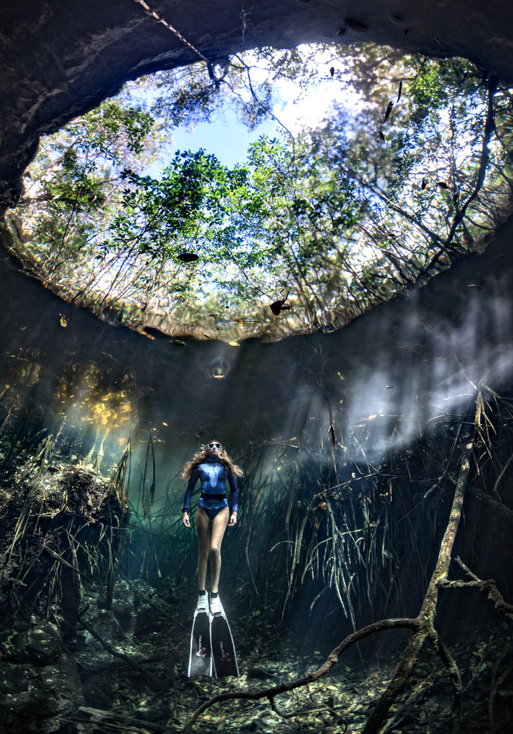 Female diver floating at the bottom of a sunlit cenote.
