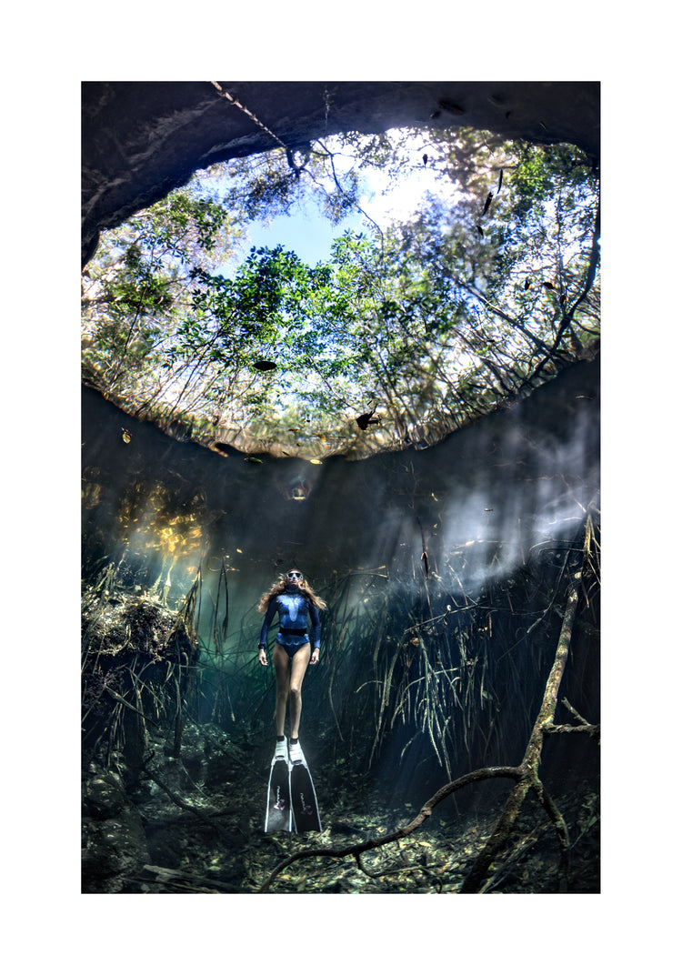 Female diver floating at the bottom of a sunlit cenote.