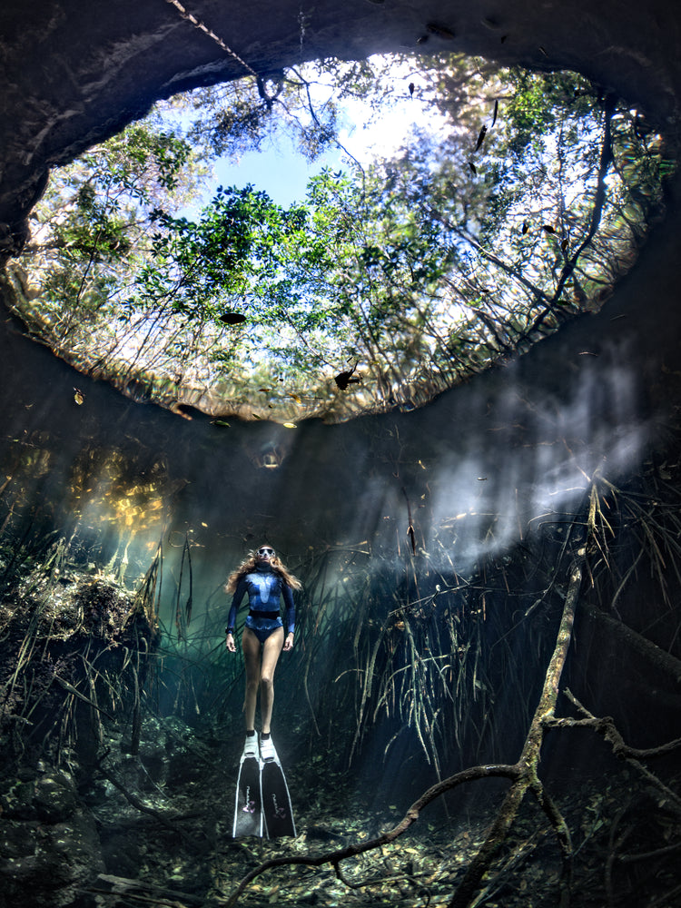 Female diver floating at the bottom of a sunlit cenote.