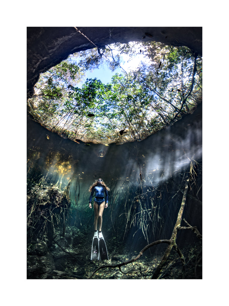 Female diver floating at the bottom of a sunlit cenote.