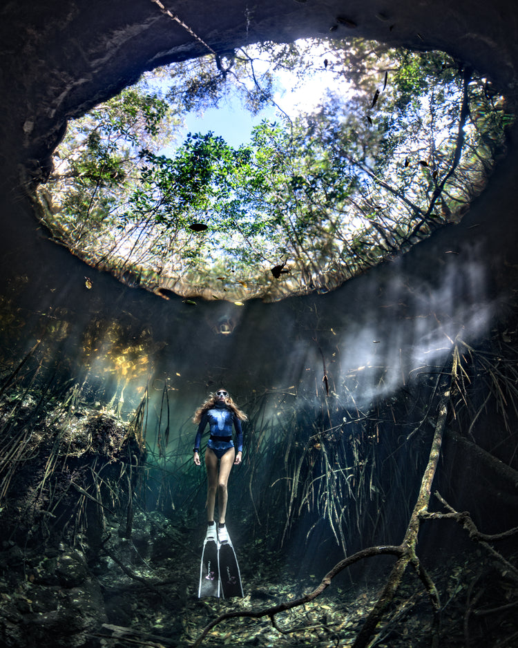 Female diver floating at the bottom of a sunlit cenote.