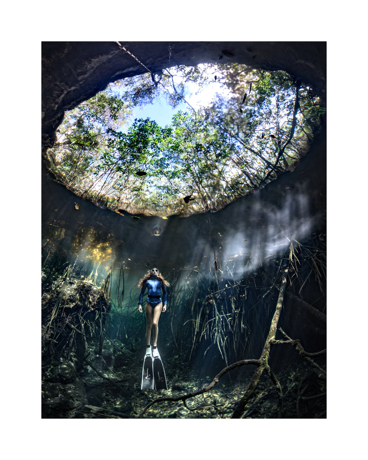 Female diver floating at the bottom of a sunlit cenote.