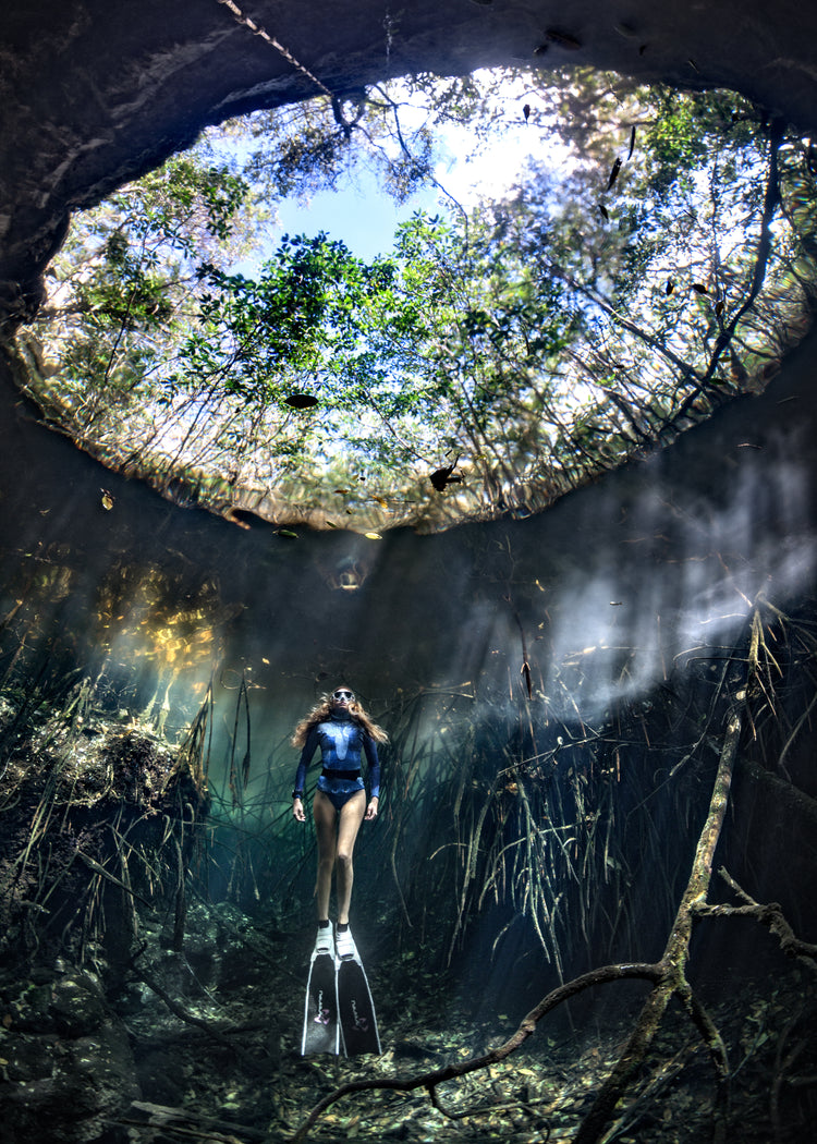 Female diver floating at the bottom of a sunlit cenote.