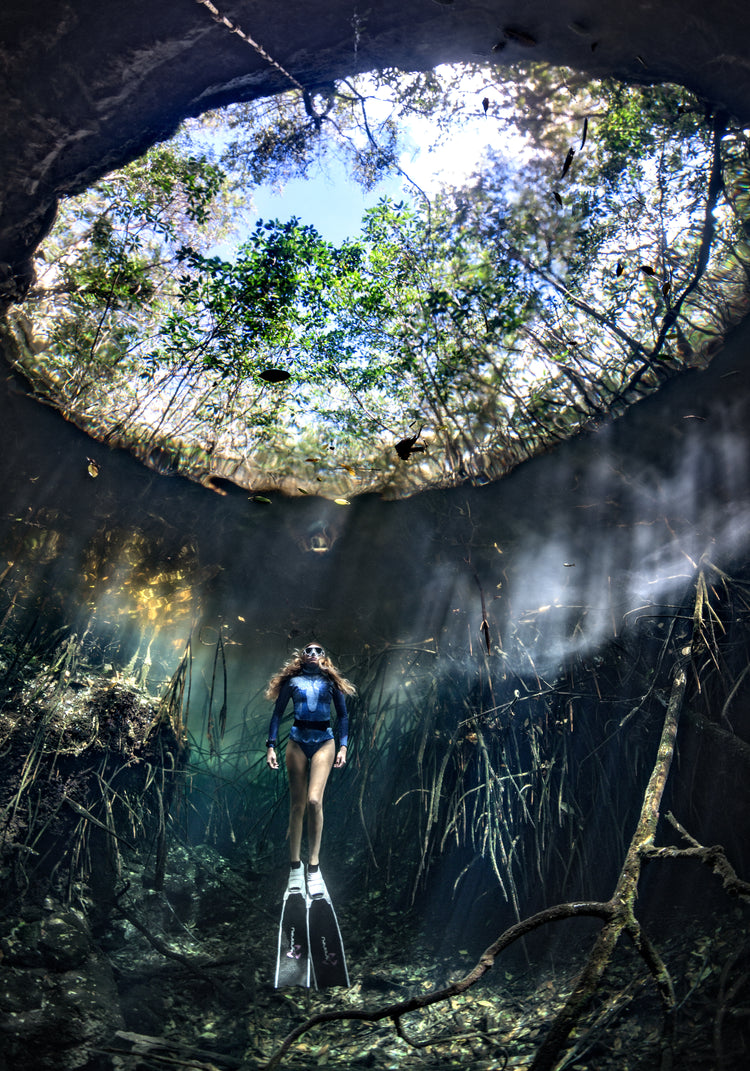 Female diver floating at the bottom of a sunlit cenote.