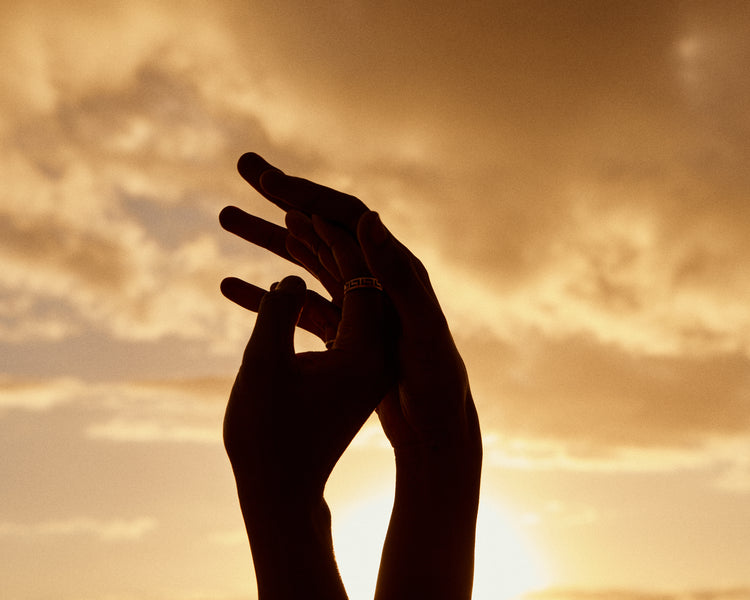 Hands grasping for each other in front of a crimson sky.