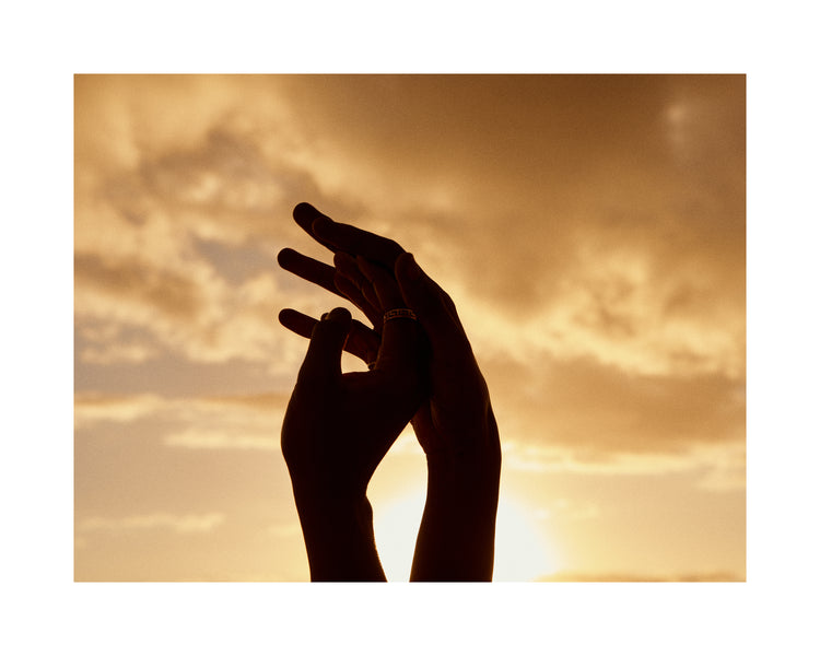 Hands grasping for each other in front of a crimson sky.