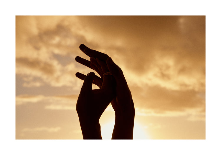 Hands grasping for each other in front of a crimson sky.