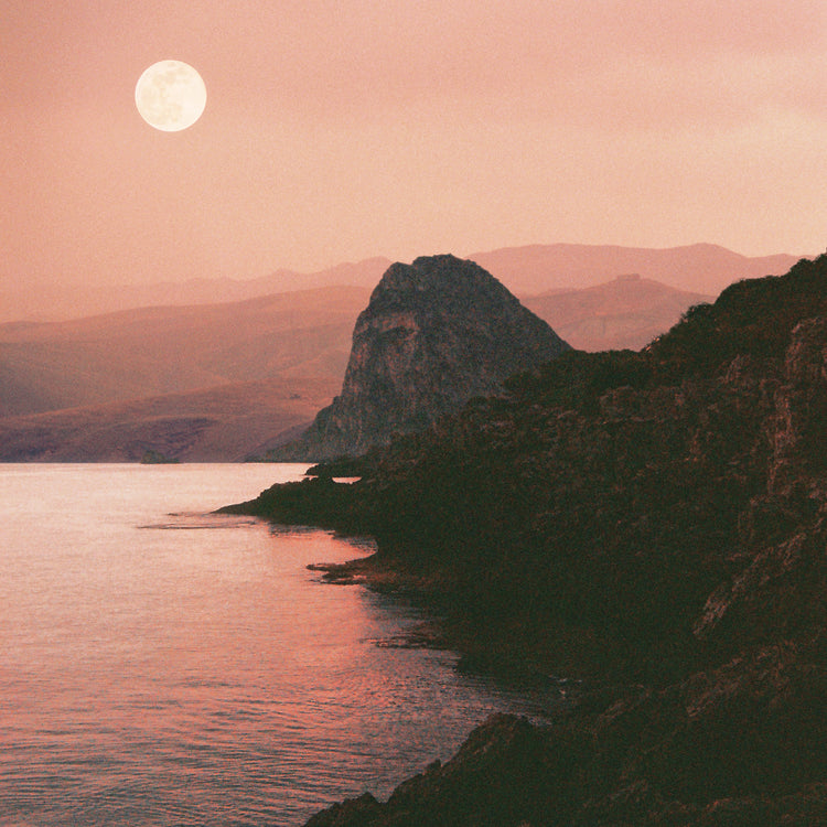 Full moon shining bright over the coastline set in a mountain scenery.