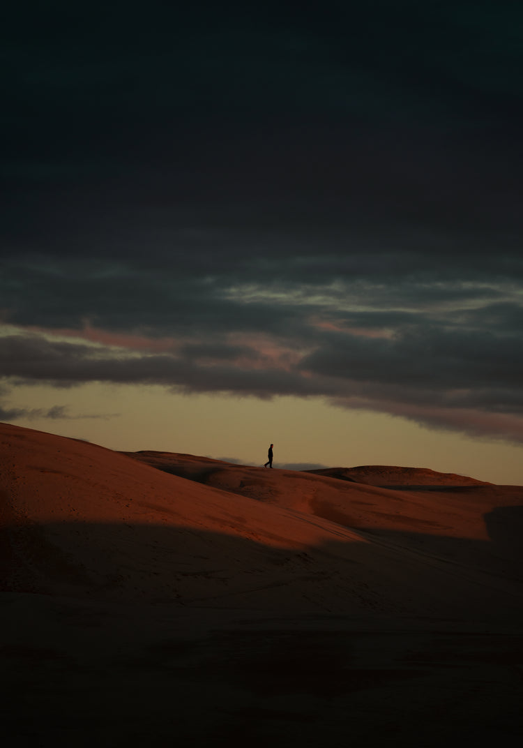 Man walking alone over orange hills in a beautiful landscape under a stormy sky.