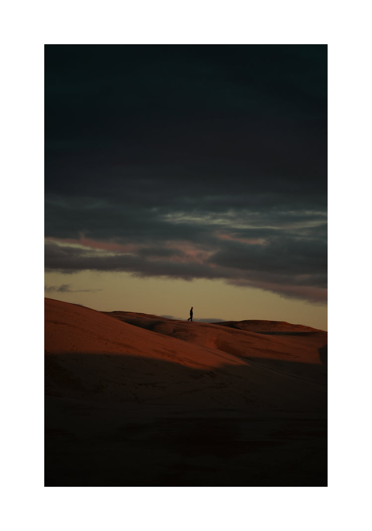 Man walking alone over orange hills in a beautiful landscape under a stormy sky.