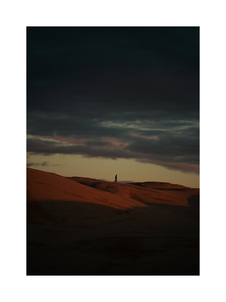 Man walking alone over orange hills in a beautiful landscape under a stormy sky.