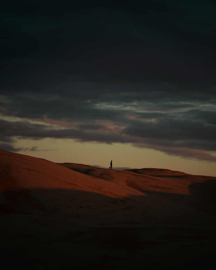 Man walking alone over orange hills in a beautiful landscape under a stormy sky.