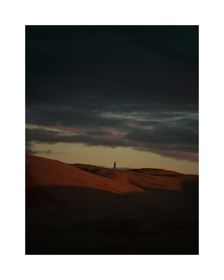 Man walking alone over orange hills in a beautiful landscape under a stormy sky.
