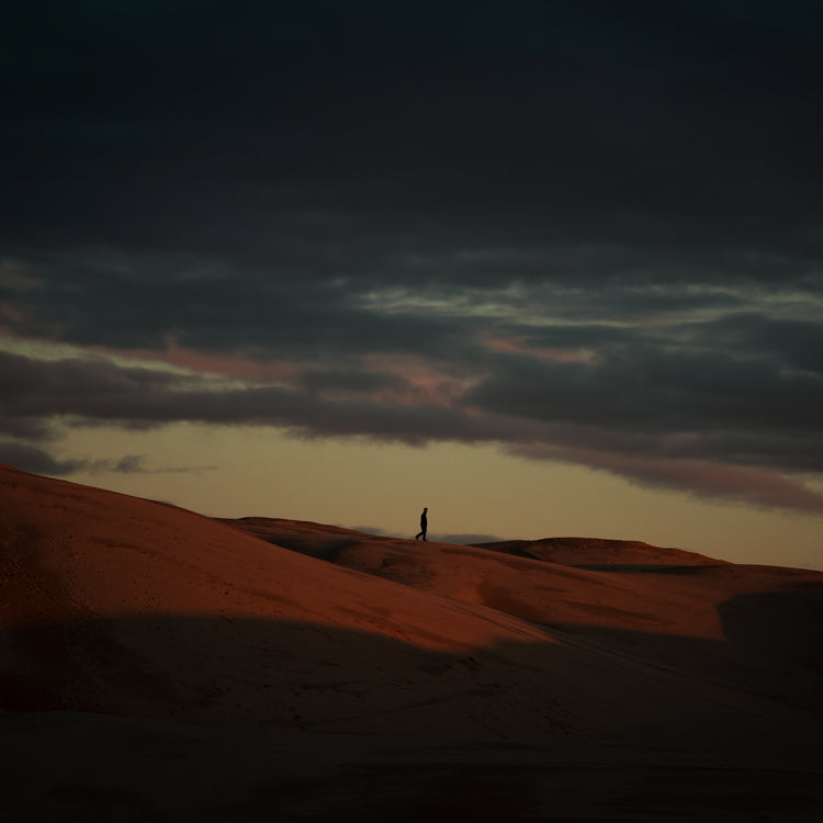 Man walking alone over orange hills in a beautiful landscape under a stormy sky.