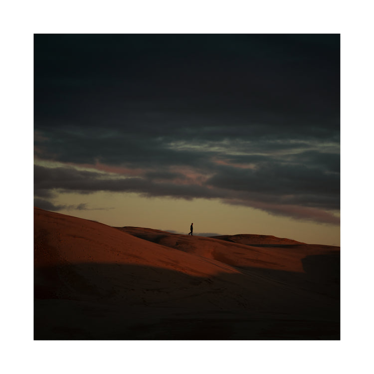Man walking alone over orange hills in a beautiful landscape under a stormy sky.