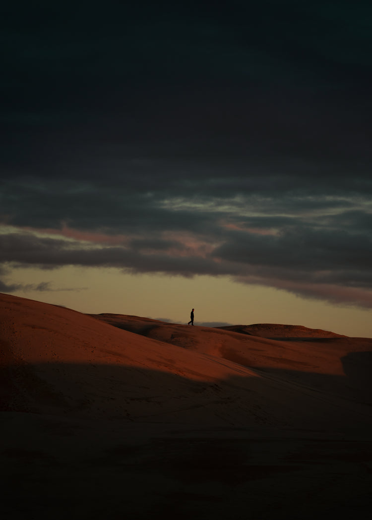 Man walking alone over orange hills in a beautiful landscape under a stormy sky.