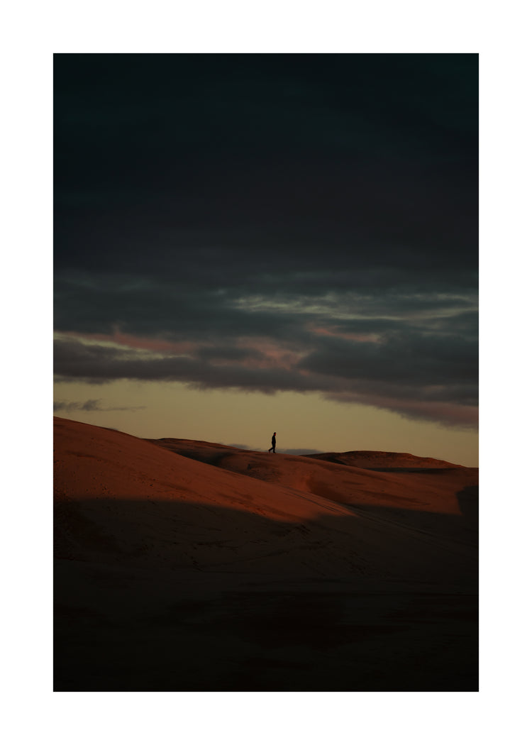 Man walking alone over orange hills in a beautiful landscape under a stormy sky.