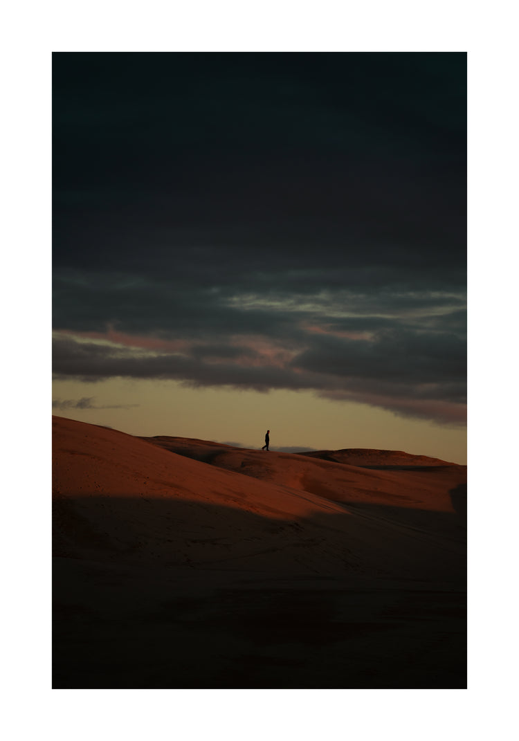 Man walking alone over orange hills in a beautiful landscape under a stormy sky.