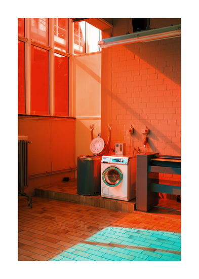 The Laundry Day Poster features a vibrant laundromat bathed in natural light, with orange and teal hues. It showcases a washing machine, outlet-fitted countertop, raised platform with a round drum and mannequin arms. The tiled floor and large windows echo Delfina Carmonas vivid style.