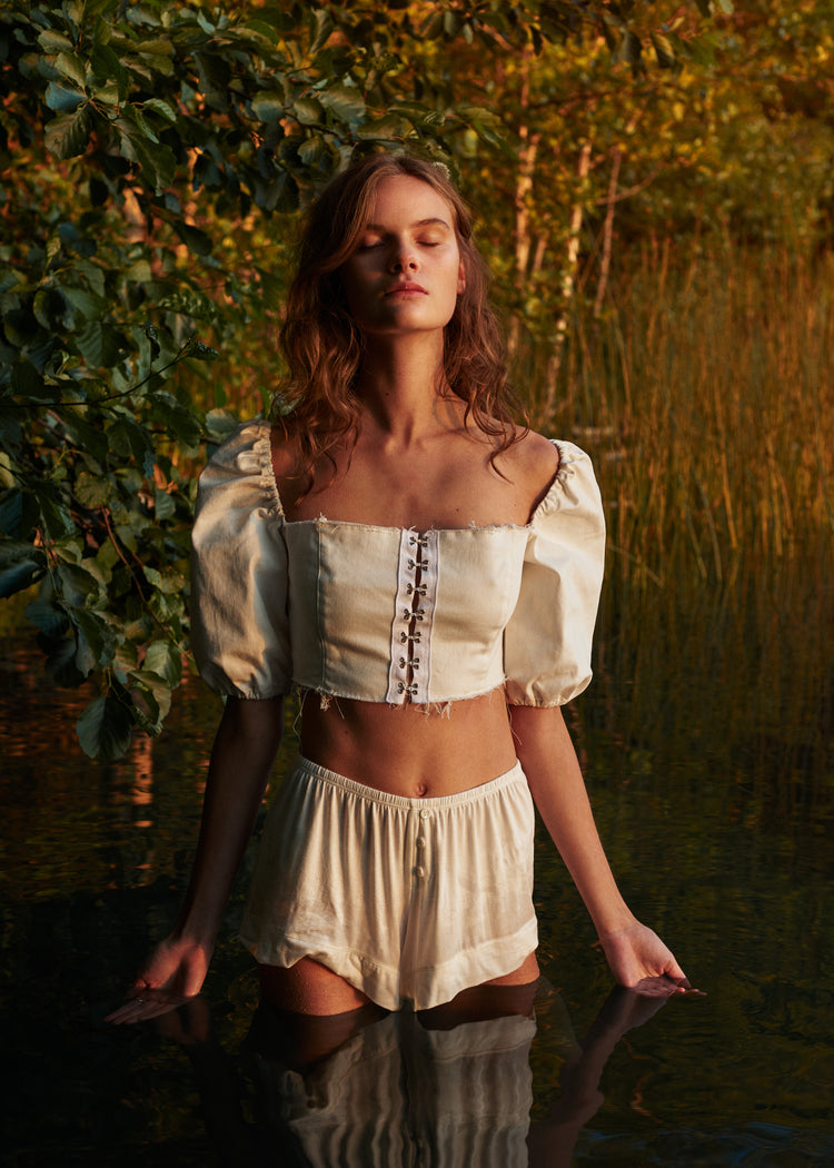 Portrait of a woman standing fully clothed in a black lake surrounded by forest.