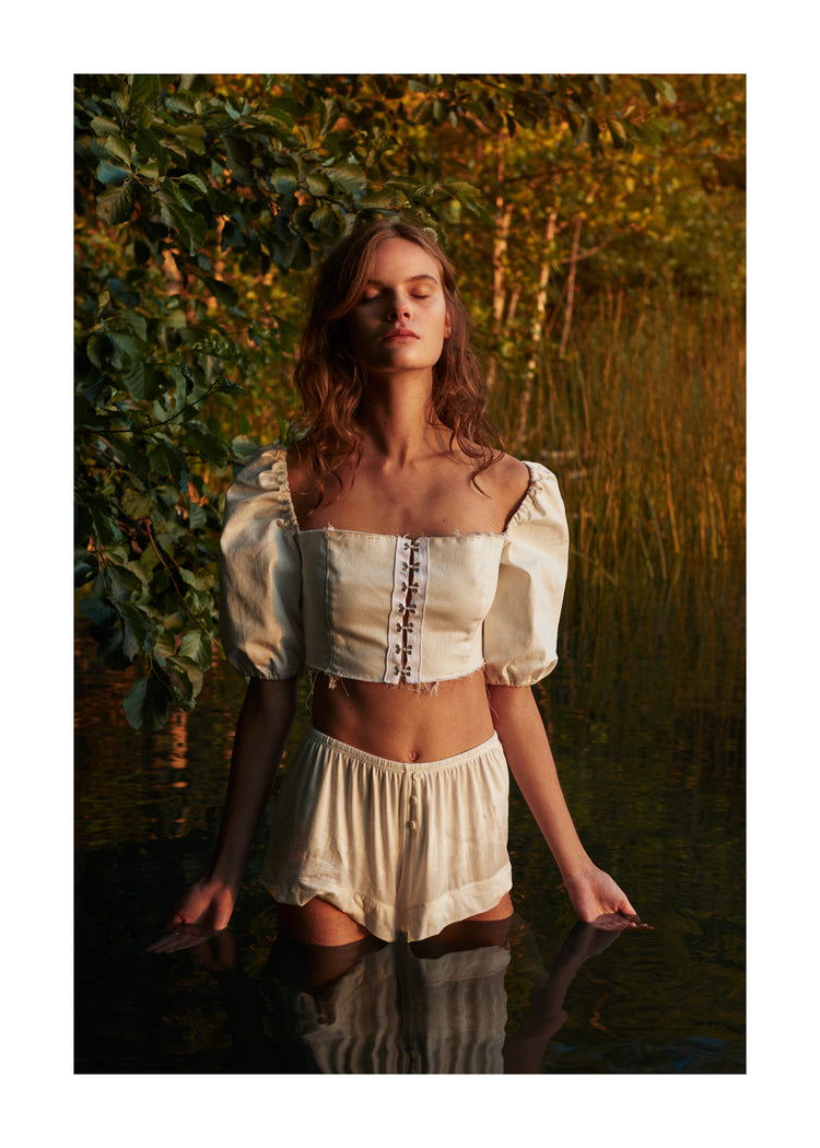 Portrait of a woman standing fully clothed in a black lake surrounded by forest.