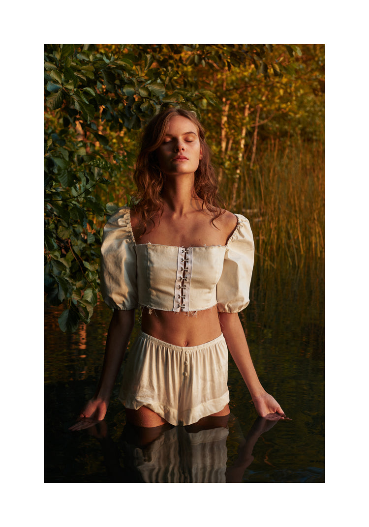 Portrait of a woman standing fully clothed in a black lake surrounded by forest.