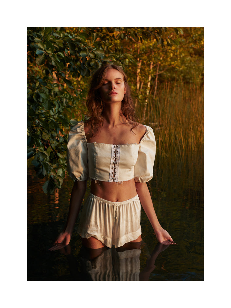 Portrait of a woman standing fully clothed in a black lake surrounded by forest.