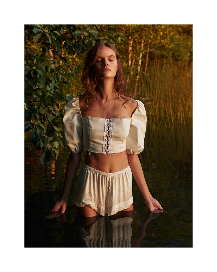Portrait of a woman standing fully clothed in a black lake surrounded by forest.