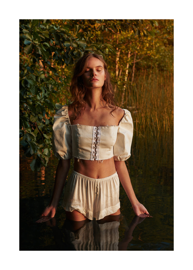 Portrait of a woman standing fully clothed in a black lake surrounded by forest.