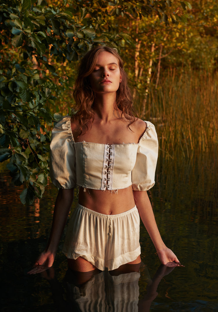 Portrait of a woman standing fully clothed in a black lake surrounded by forest.