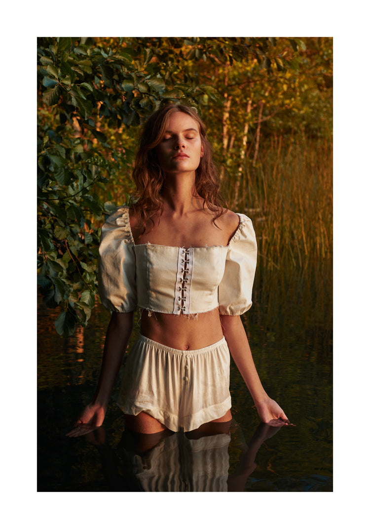 Portrait of a woman standing fully clothed in a black lake surrounded by forest.