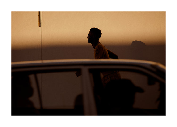 Man dressed in beige running in the opposite direction of a car in front of him.