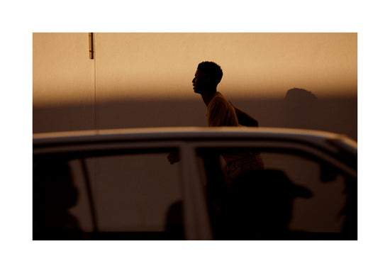 Man dressed in beige running in the opposite direction of a car in front of him.