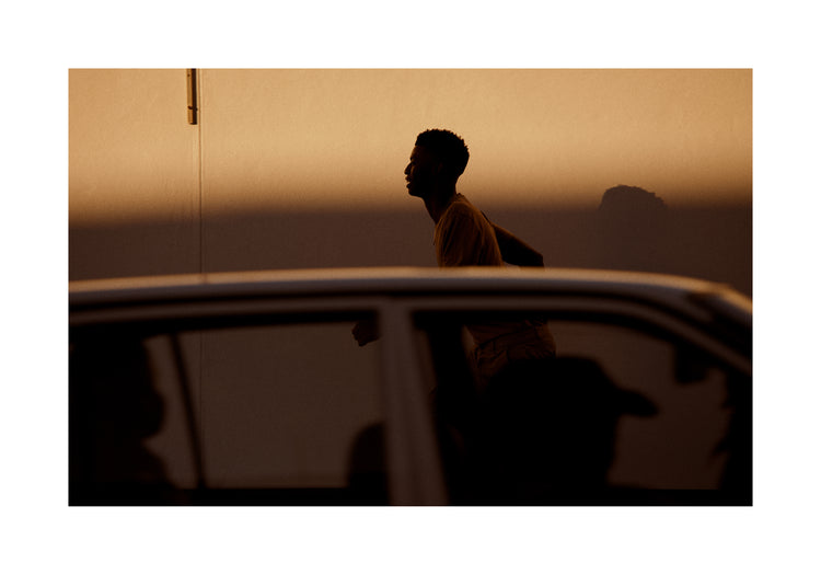 Man dressed in beige running in the opposite direction of a car in front of him.
