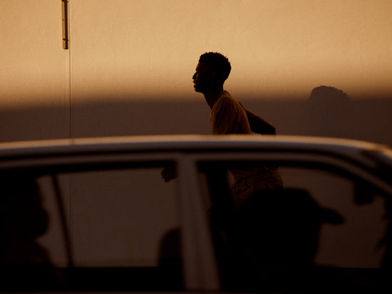 Man dressed in beige running in the opposite direction of a car in front of him.