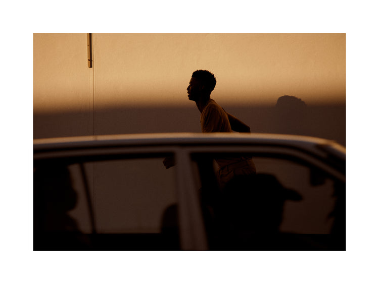 Man dressed in beige running in the opposite direction of a car in front of him.