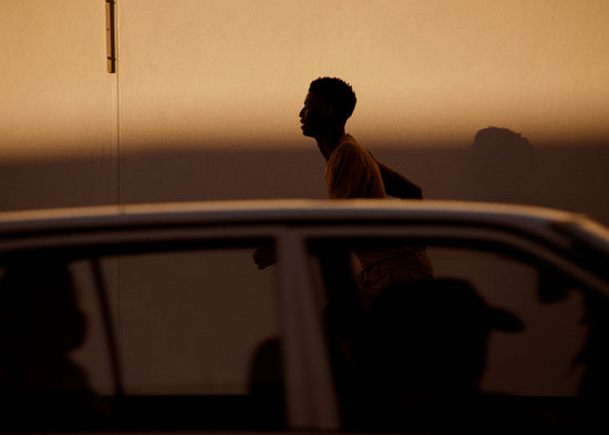 Man dressed in beige running in the opposite direction of a car in front of him.