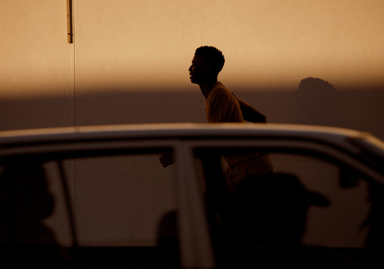 Man dressed in beige running in the opposite direction of a car in front of him.