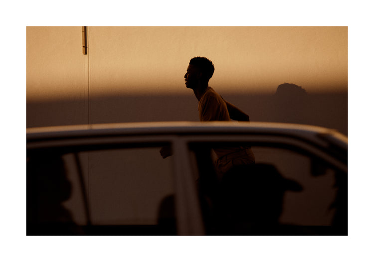 Man dressed in beige running in the opposite direction of a car in front of him.
