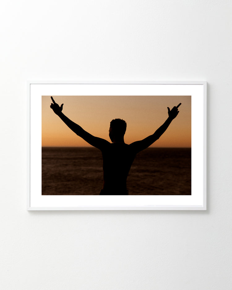 A poster titled My New Tinder Picture depicts a silhouette of a person with raised arms against an orange sunset, framed boldly on a white wall.
