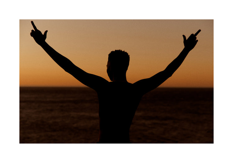 Man standing in front of a sea at sunset and flipping everybody off.