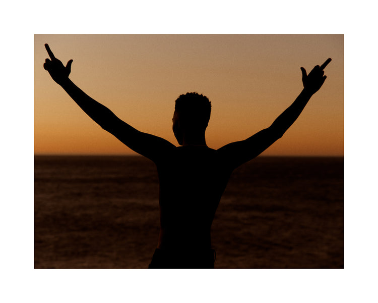 Man standing in front of a sea at sunset and flipping everybody off.