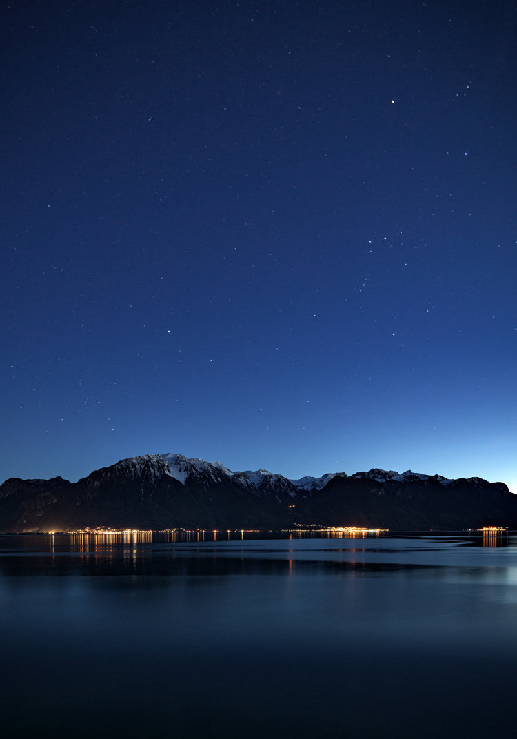 Mountain scenery, lights from a city and a lake under a star strewn sky.