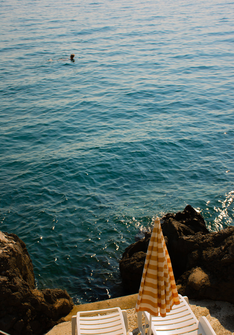 Tanning beds and a beach umbrella on the shore of the blue, Croatian sea.