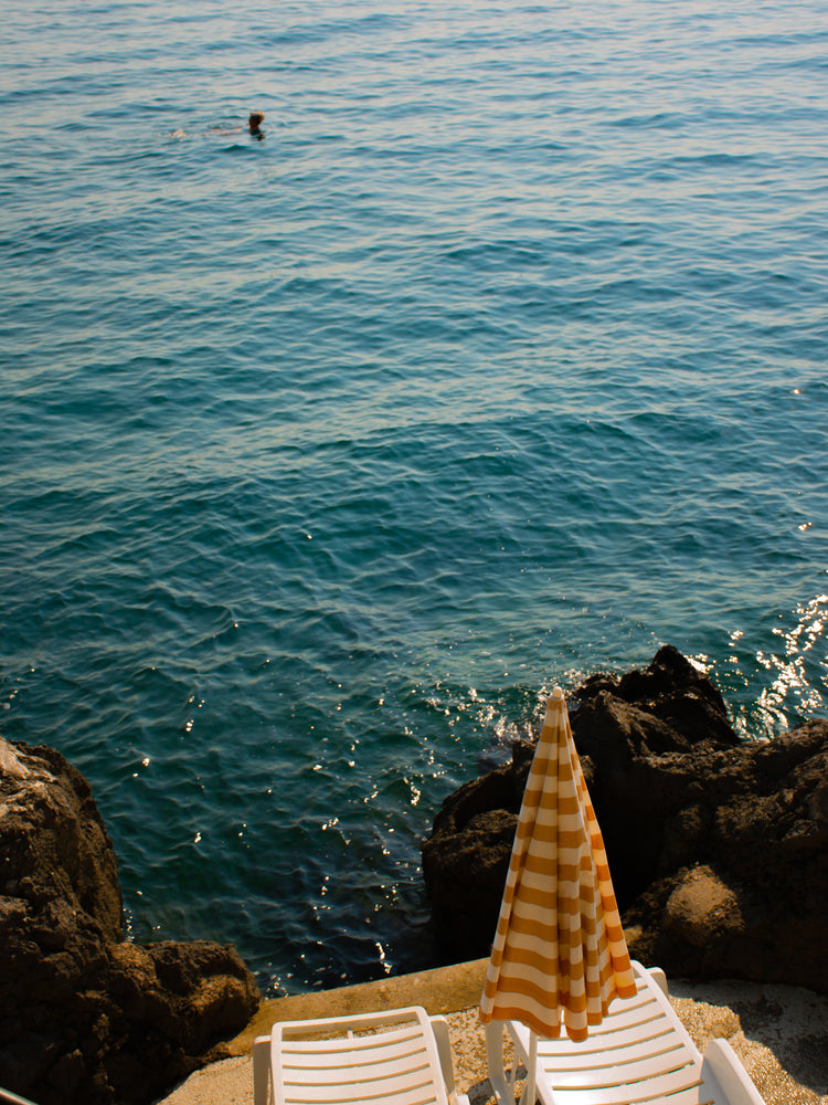 Tanning beds and a beach umbrella on the shore of the blue, Croatian sea.