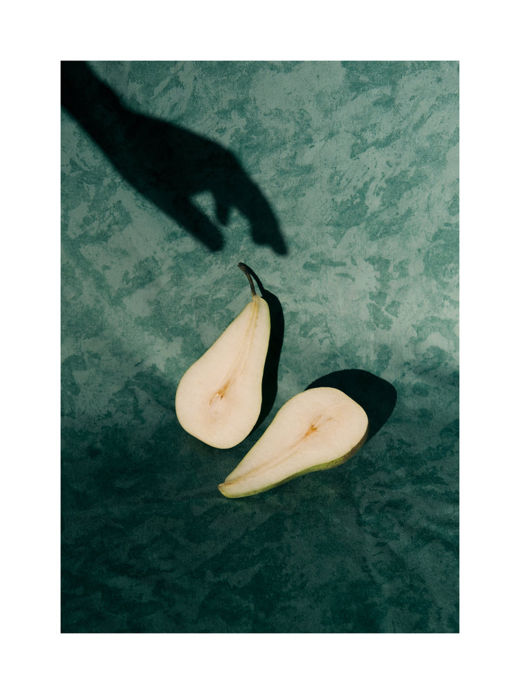 Still life of a pear cut in half and a shadow of a hand reaching for it.