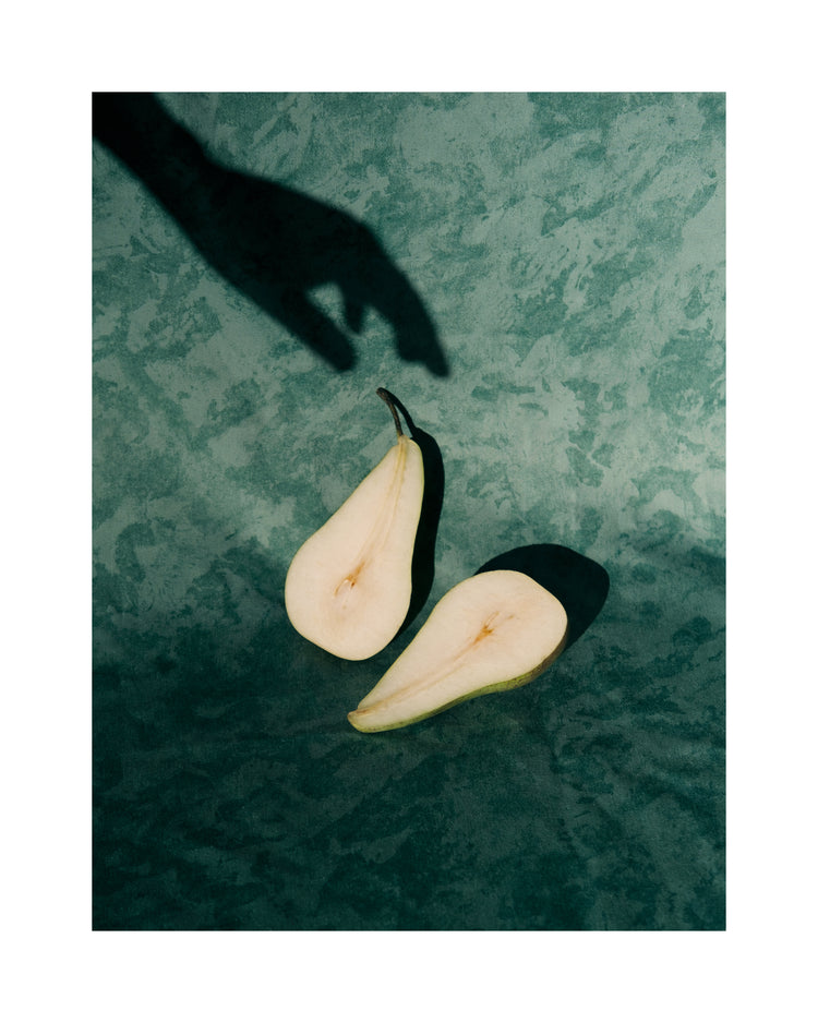 Still life of a pear cut in half and a shadow of a hand reaching for it.