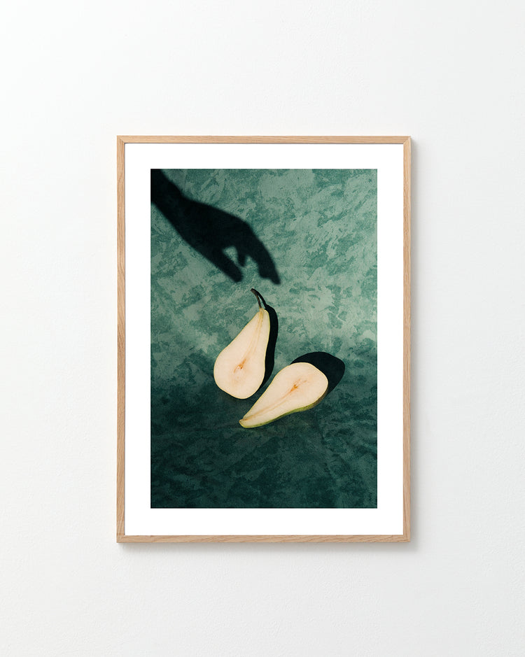 Still life of a pear cut in half and a shadow of a hand reaching for it.