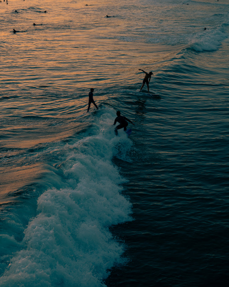 Surfers playing in the last waves of the day as the sun goes down.